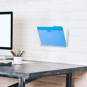Wall-mounted plastic hanging wall file holding a blue folder on a white brick wall near a desk.