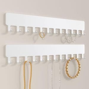 White, wall-mounted flat metal bar that has hooks along the bottom to hold jewelry.