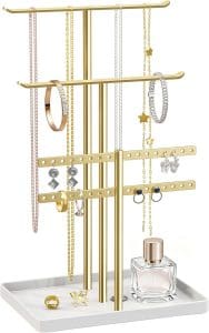 A gold jewelry stand that has metal bars at various heights to hold necklaces, bracelets and earrings, with a white base at the bottom.