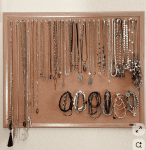 A bulletin board with necklaces and bracelets hanging from tacks that have been lined up horizontally.