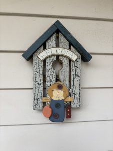 Image of a outside decoration that says "welcome" and has a scarecrow decoration hanging on the front.
